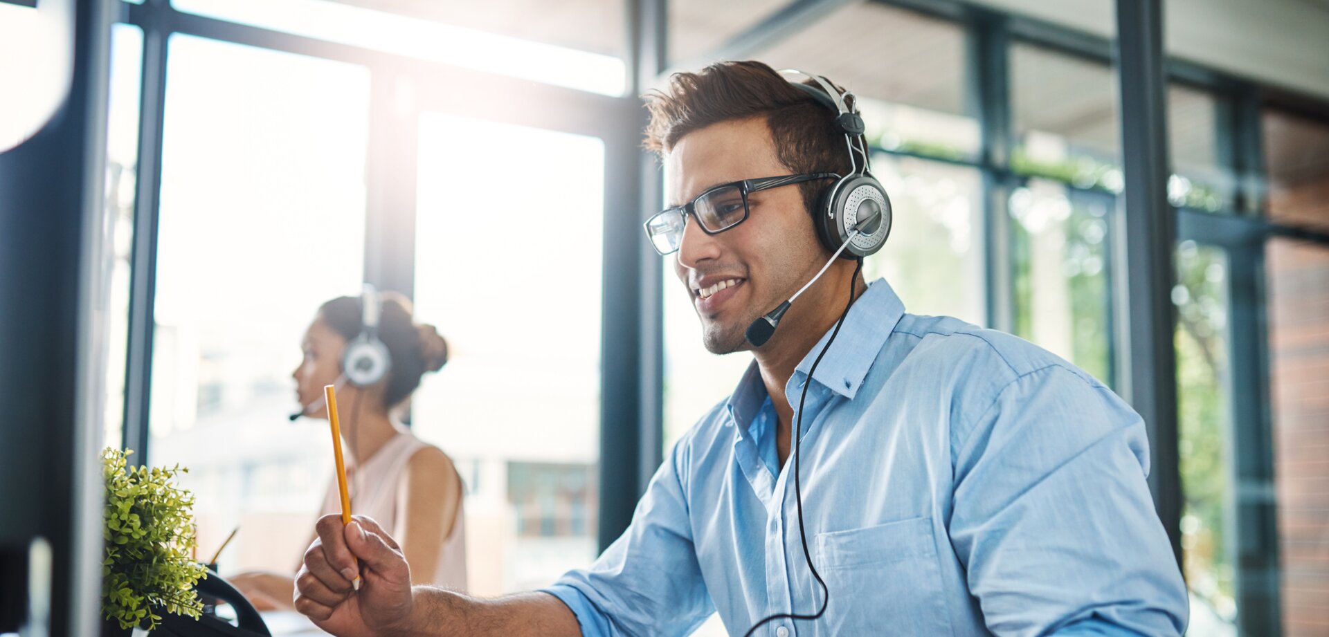 © iStock-1132874986_PeopleImages (Cropped shot of a handsome young man working in a call center with a female colleague in the background)